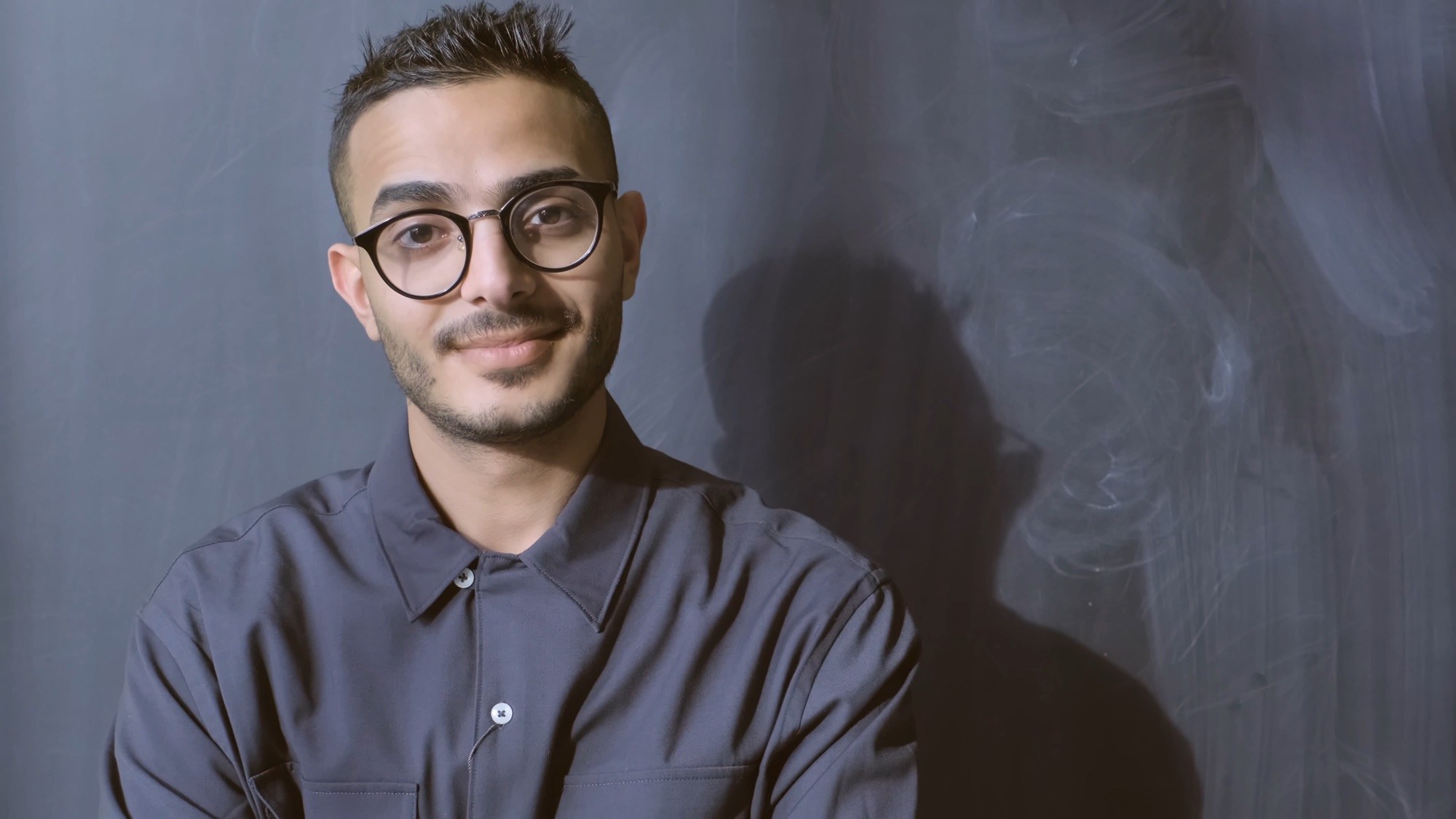 Student in glasses smiling against a chalkboard wall
